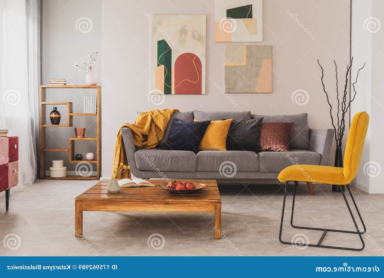Favorite Wooden Coffee Table And Yellow Chair In Front Of Grey Couch With Pillows In  Trendy Living Room Stock Image – Image Of Living, Gallery: 175962989 In Cushioned Chair Loveseat Tables (Photo 14 of 15)